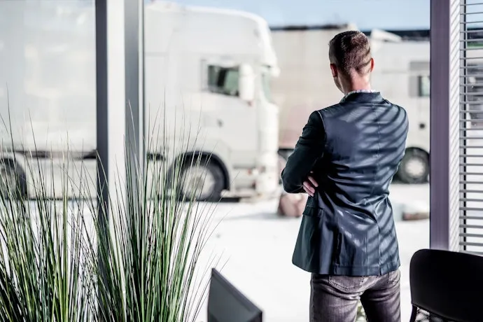 Businessman looking out the window at a truck in a courtyard.